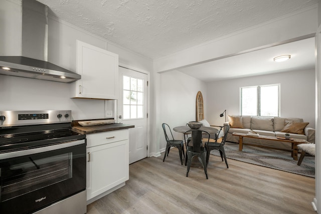 kitchen with a healthy amount of sunlight, wall chimney exhaust hood, stainless steel range with electric stovetop, and white cabinetry