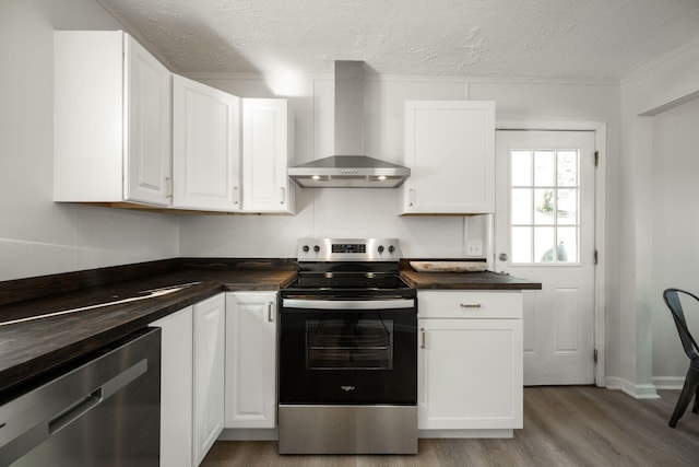 kitchen with white cabinets, a textured ceiling, light hardwood / wood-style flooring, wall chimney range hood, and appliances with stainless steel finishes