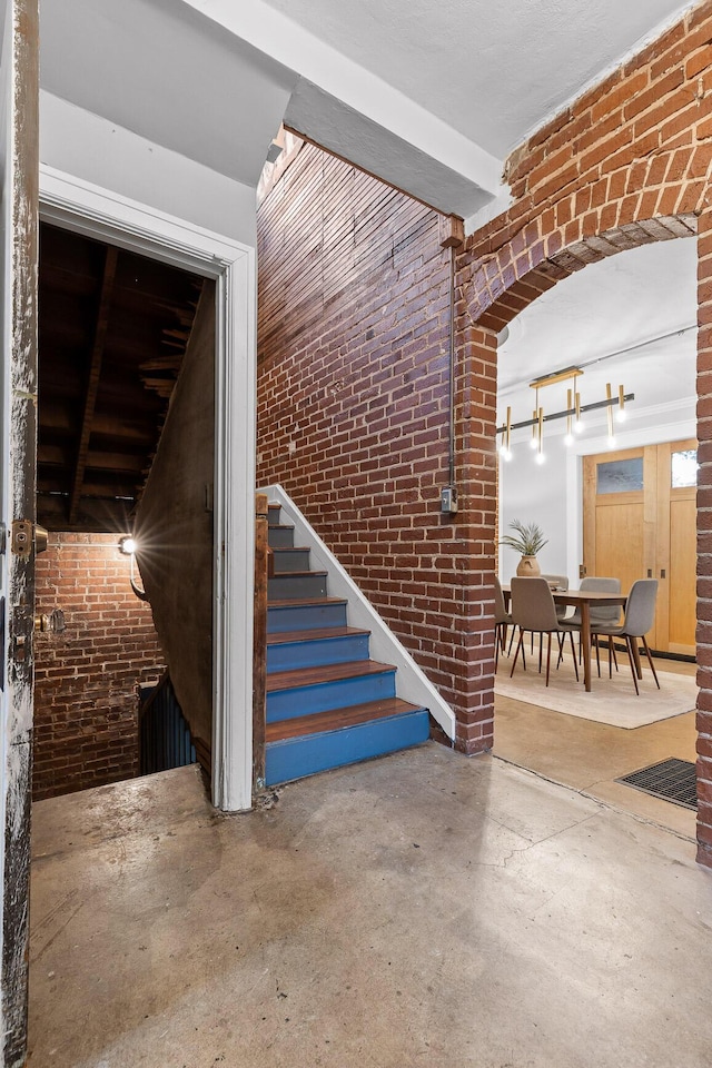 staircase featuring concrete flooring and brick wall