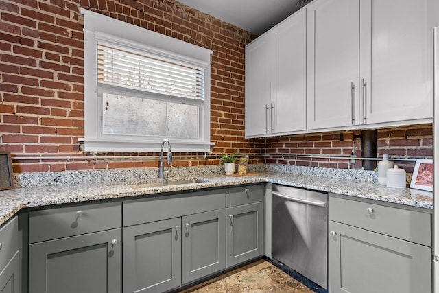 kitchen with dishwasher, sink, light stone counters, brick wall, and gray cabinets