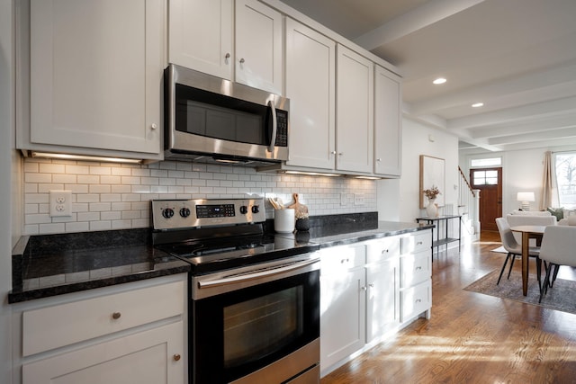 kitchen with white cabinetry, light hardwood / wood-style flooring, backsplash, dark stone counters, and appliances with stainless steel finishes