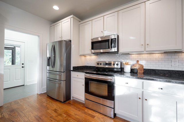 kitchen with white cabinetry, stainless steel appliances, tasteful backsplash, dark stone counters, and wood-type flooring