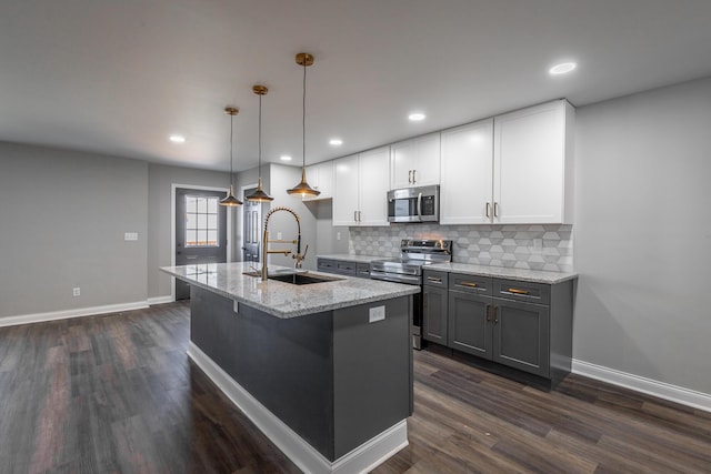 kitchen featuring light stone countertops, stainless steel appliances, sink, white cabinets, and hanging light fixtures