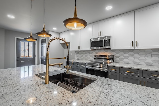 kitchen with light stone countertops, appliances with stainless steel finishes, tasteful backsplash, pendant lighting, and white cabinetry