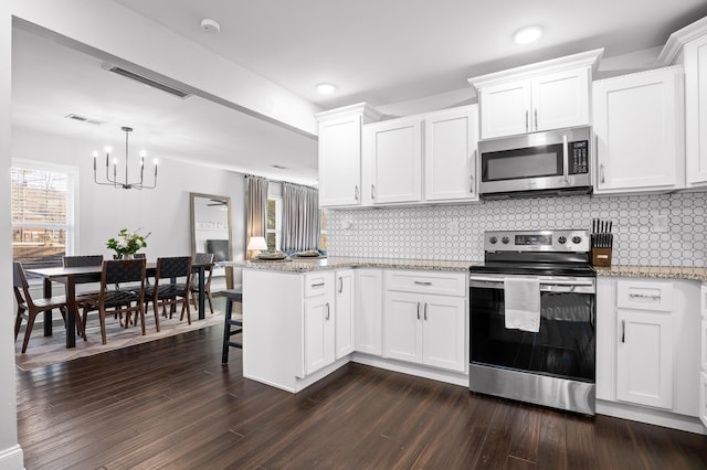 kitchen featuring visible vents, decorative backsplash, appliances with stainless steel finishes, a peninsula, and an inviting chandelier