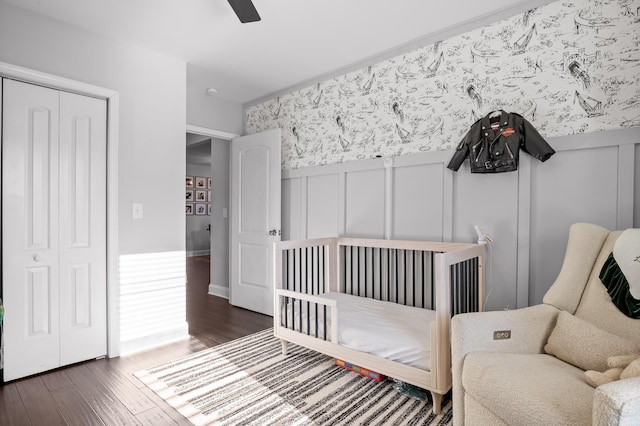 bedroom with wallpapered walls, ceiling fan, wainscoting, wood finished floors, and a decorative wall