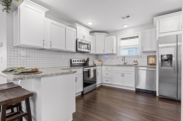 kitchen with visible vents, appliances with stainless steel finishes, white cabinets, light stone countertops, and dark wood-style flooring