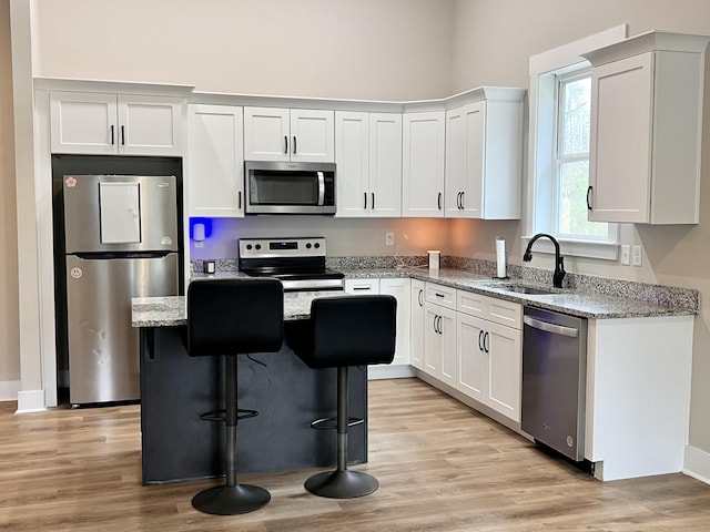 kitchen with a center island, sink, light stone countertops, white cabinetry, and stainless steel appliances