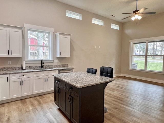 kitchen with a kitchen bar, light wood-type flooring, sink, white cabinets, and a center island