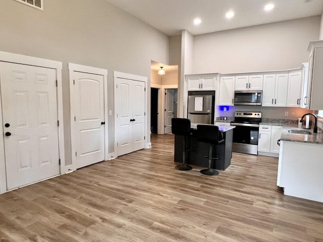 kitchen featuring stainless steel appliances, a kitchen island, sink, high vaulted ceiling, and white cabinetry