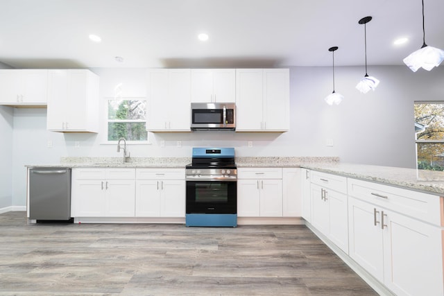 kitchen featuring white cabinets, appliances with stainless steel finishes, light wood-type flooring, and pendant lighting