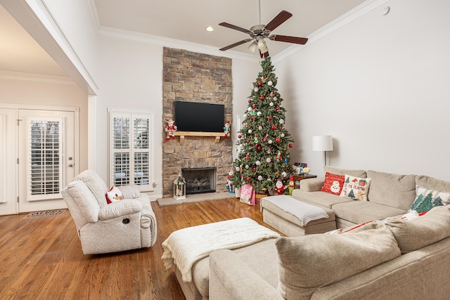 living room featuring hardwood / wood-style flooring, ceiling fan, a stone fireplace, and crown molding