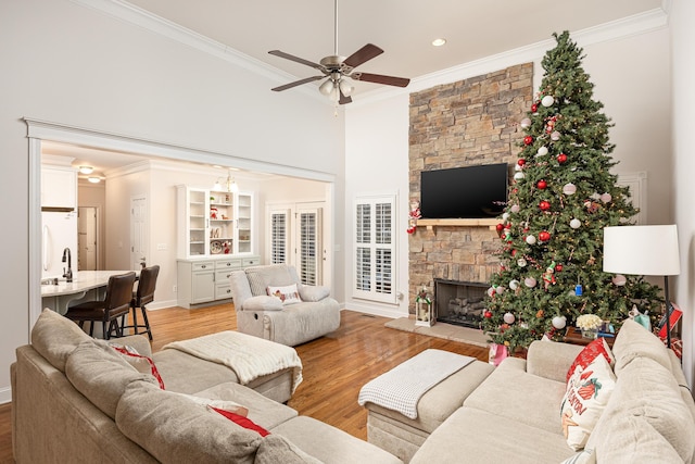 living room with a fireplace, light hardwood / wood-style flooring, ceiling fan, and crown molding