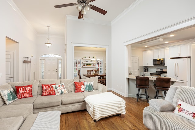 living room featuring a towering ceiling, ornamental molding, ceiling fan, dark wood-type flooring, and sink