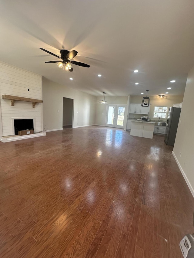 unfurnished living room with dark hardwood / wood-style flooring, a fireplace, ceiling fan, and a healthy amount of sunlight