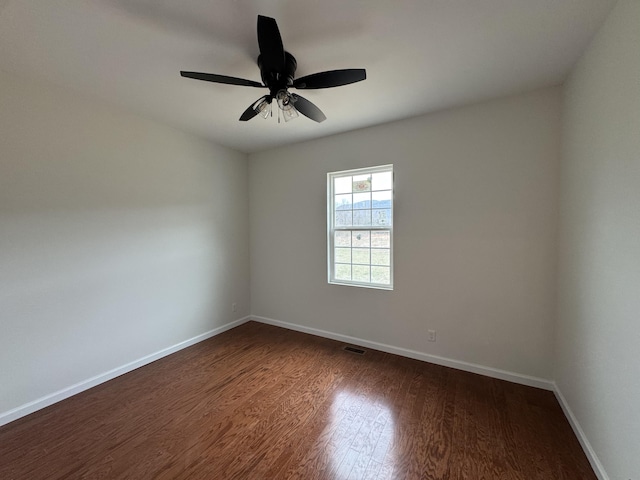 empty room with dark wood-style floors, ceiling fan, visible vents, and baseboards