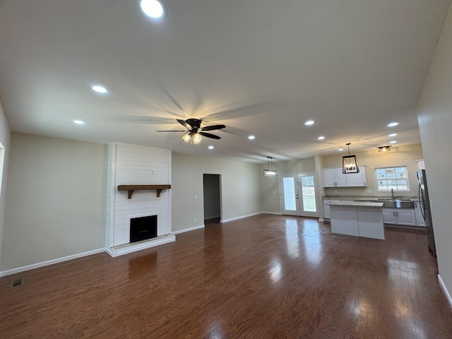 unfurnished living room with ceiling fan, a large fireplace, and dark hardwood / wood-style floors