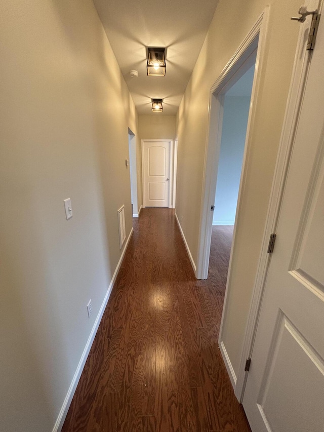 corridor with dark wood-type flooring, visible vents, and baseboards