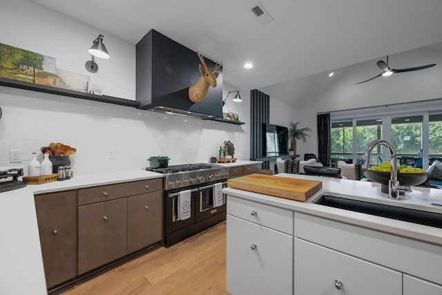 kitchen with lofted ceiling, exhaust hood, range with two ovens, light hardwood / wood-style flooring, and dark brown cabinets