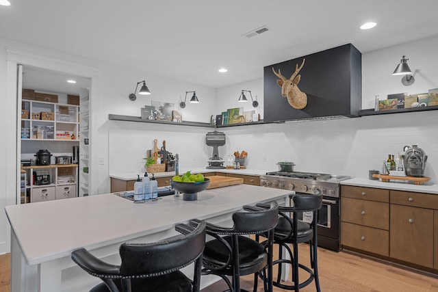 kitchen with stainless steel range, a center island, wall chimney range hood, light hardwood / wood-style flooring, and backsplash