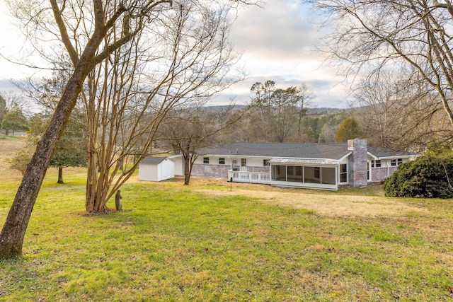 rear view of house with a sunroom, a storage shed, and a yard