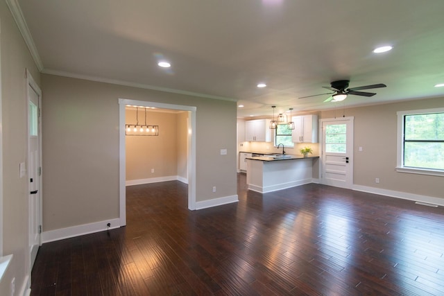 unfurnished living room featuring ceiling fan with notable chandelier, dark hardwood / wood-style flooring, crown molding, and sink