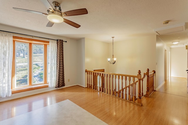 empty room featuring ceiling fan with notable chandelier, a textured ceiling, and light hardwood / wood-style flooring