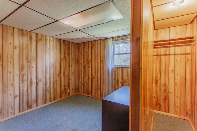 carpeted empty room featuring a paneled ceiling and wood walls