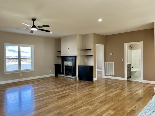 unfurnished living room featuring a stone fireplace, ceiling fan, and hardwood / wood-style flooring