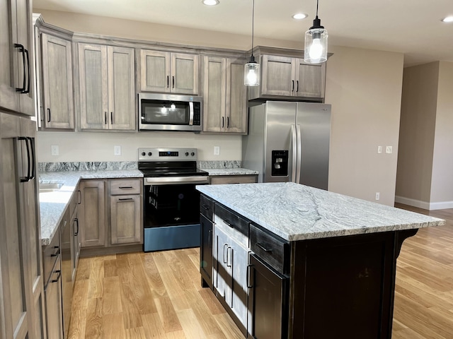 kitchen featuring light stone countertops, appliances with stainless steel finishes, light wood-type flooring, a center island, and hanging light fixtures