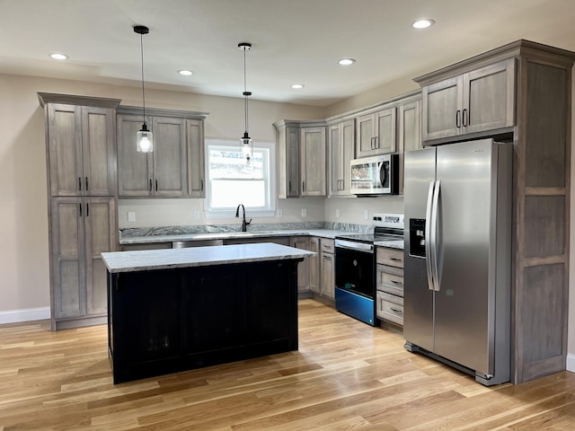 kitchen featuring sink, a center island, hanging light fixtures, appliances with stainless steel finishes, and light wood-type flooring