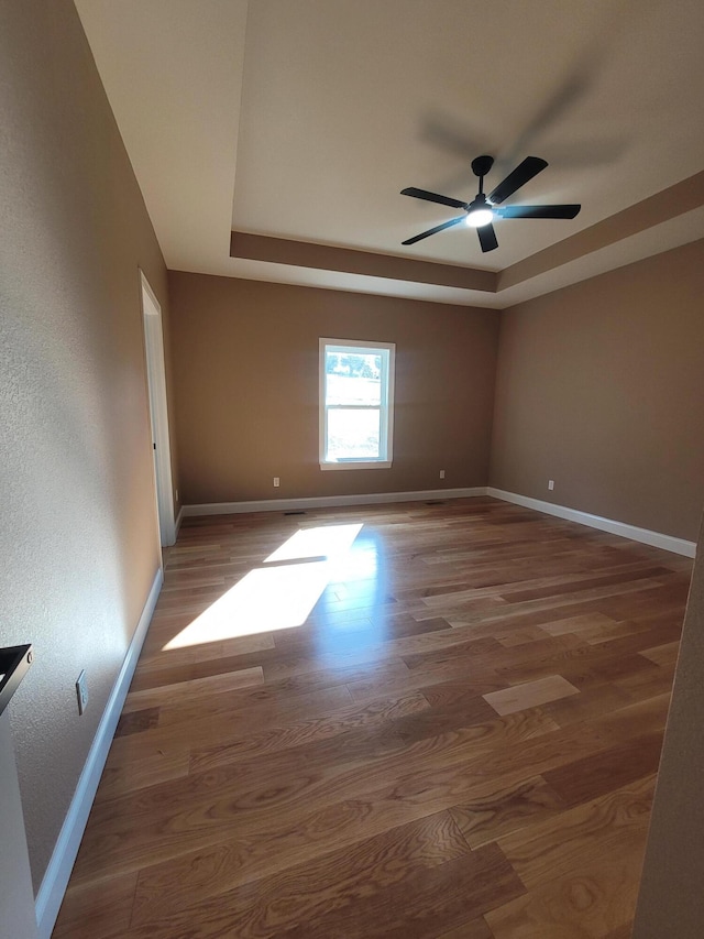 empty room featuring wood-type flooring, a raised ceiling, and ceiling fan