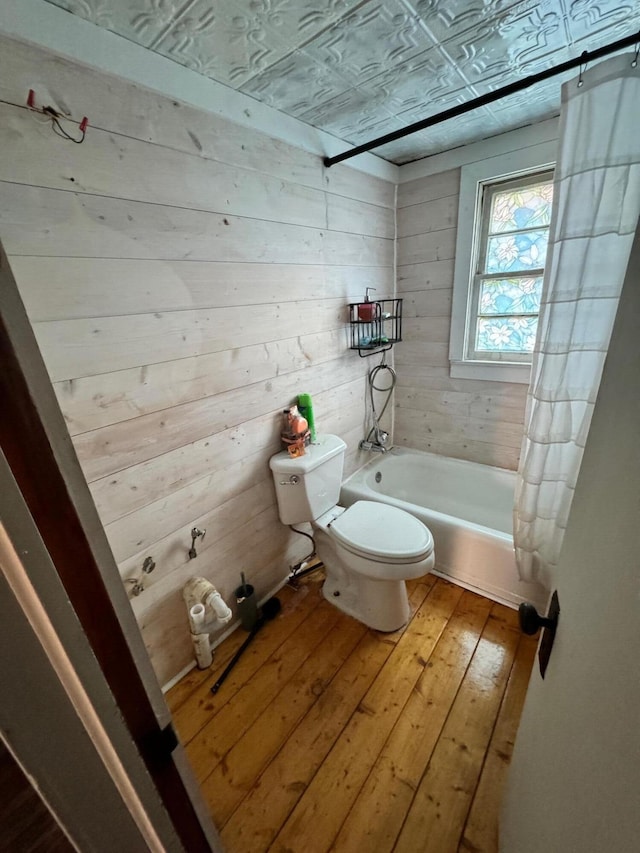 bathroom with wooden walls, shower / tub combo with curtain, wood-type flooring, and toilet