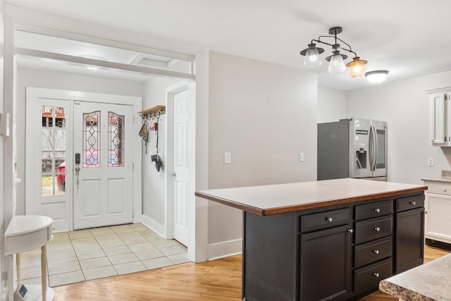 kitchen featuring a kitchen island, stainless steel refrigerator with ice dispenser, pendant lighting, white cabinets, and light wood-type flooring