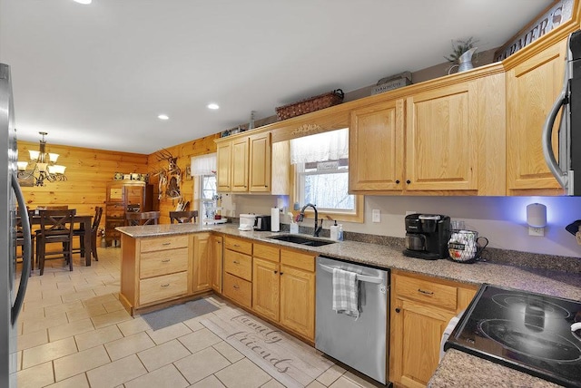 kitchen with sink, stainless steel appliances, kitchen peninsula, a chandelier, and wooden walls