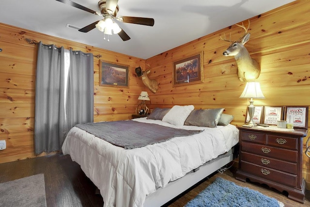 bedroom with ceiling fan, dark hardwood / wood-style flooring, and wooden walls