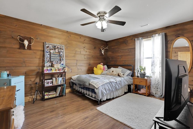 bedroom featuring ceiling fan, wooden walls, and wood-type flooring