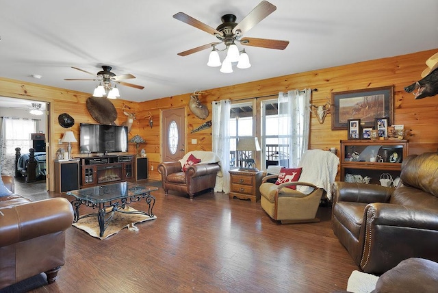 living room with ceiling fan, dark wood-type flooring, and wooden walls