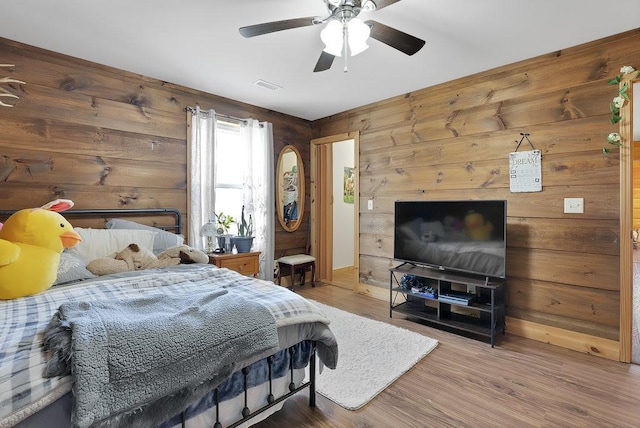 bedroom with wood-type flooring, ceiling fan, and wooden walls