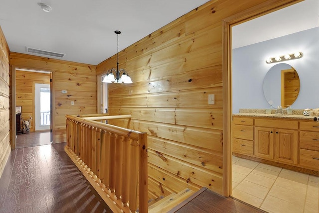 hall with light wood-type flooring, wooden walls, and a notable chandelier