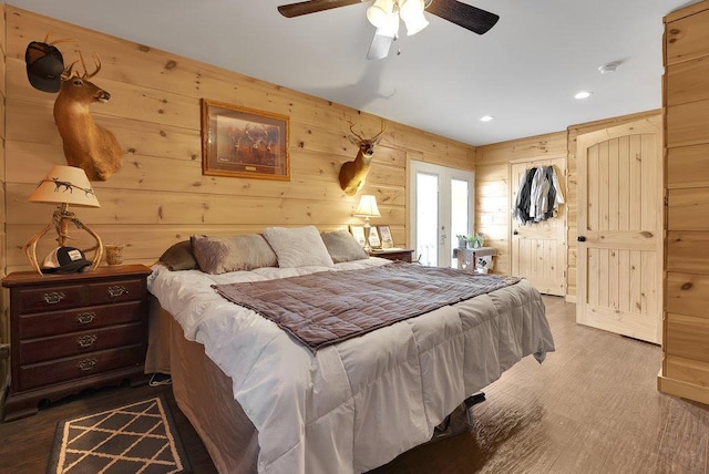 bedroom with hardwood / wood-style floors, ceiling fan, and wooden walls