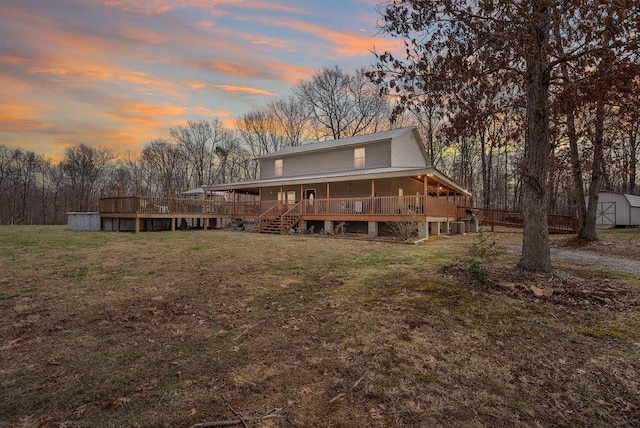 back house at dusk with a yard, a deck, and a storage unit