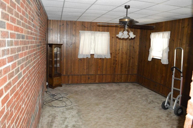 empty room with carpet, a paneled ceiling, and wooden walls