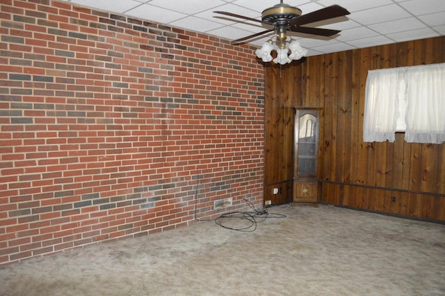 spare room featuring carpet flooring, a paneled ceiling, wood walls, and ceiling fan