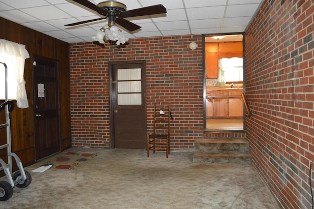 interior space with a drop ceiling, ceiling fan, carpet floors, and brick wall