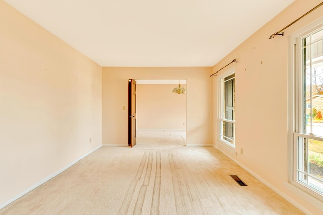 carpeted empty room with plenty of natural light and a chandelier