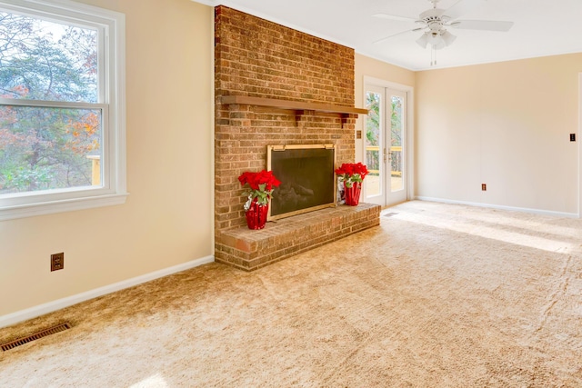 unfurnished living room featuring carpet flooring, ceiling fan, french doors, and a brick fireplace