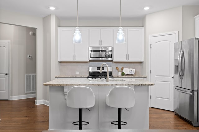 kitchen featuring white cabinetry, hanging light fixtures, light stone counters, stainless steel appliances, and a center island with sink