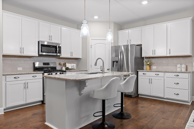 kitchen with sink, a center island with sink, appliances with stainless steel finishes, pendant lighting, and white cabinets