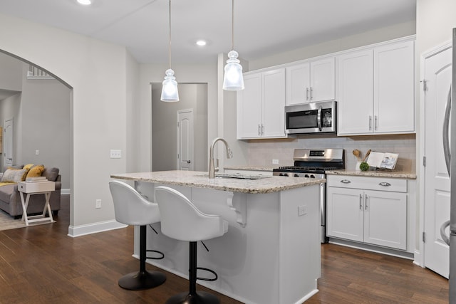 kitchen featuring hanging light fixtures, appliances with stainless steel finishes, a kitchen island with sink, and white cabinets